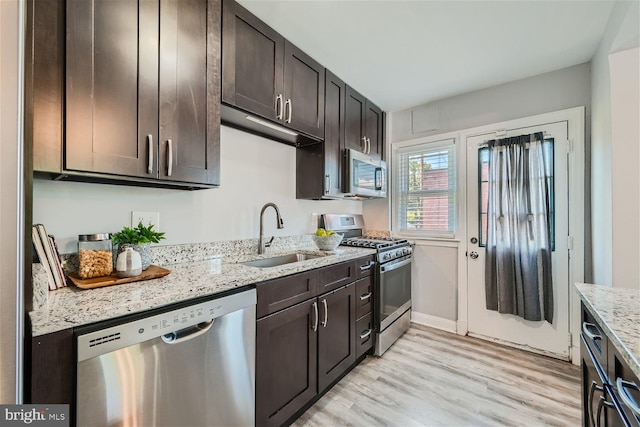 kitchen with light stone countertops, light wood-type flooring, stainless steel appliances, dark brown cabinetry, and sink