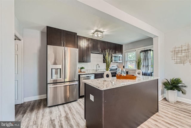 kitchen with light hardwood / wood-style floors, a kitchen island, stainless steel appliances, light stone counters, and dark brown cabinetry