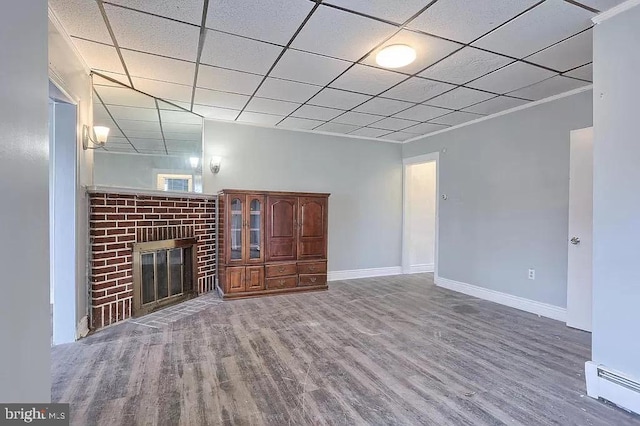 unfurnished living room with a brick fireplace, baseboard heating, hardwood / wood-style flooring, and a paneled ceiling