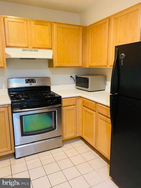 kitchen featuring stainless steel gas range oven, black fridge, and light tile patterned floors