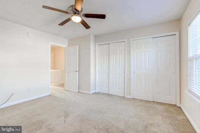 unfurnished bedroom with light carpet, two closets, and ceiling fan