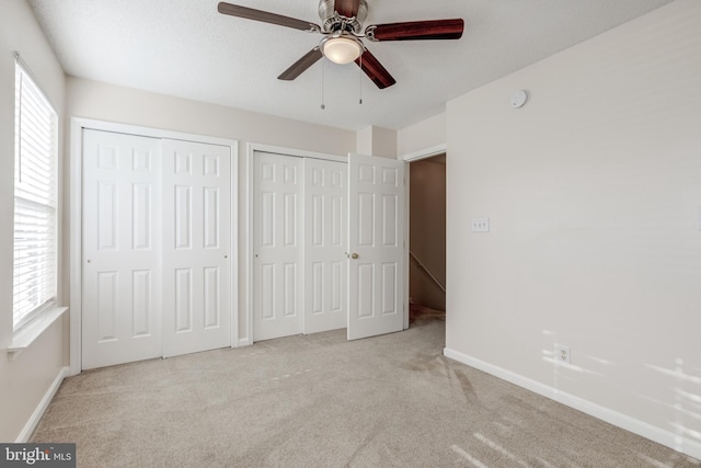 unfurnished bedroom featuring light carpet, two closets, and ceiling fan