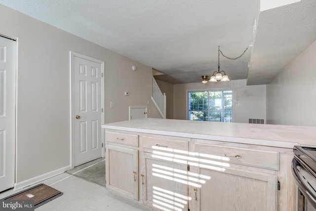 kitchen with decorative light fixtures, stainless steel stove, light brown cabinetry, and a textured ceiling