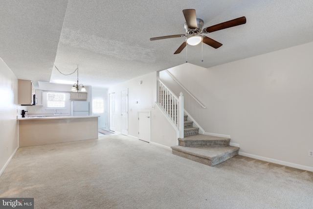 unfurnished living room featuring light carpet, a textured ceiling, and ceiling fan with notable chandelier