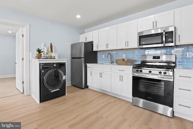 kitchen featuring tasteful backsplash, light wood-type flooring, washer / clothes dryer, white cabinetry, and appliances with stainless steel finishes