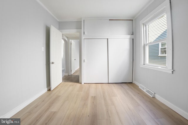 unfurnished bedroom featuring a closet, light hardwood / wood-style floors, and ornamental molding