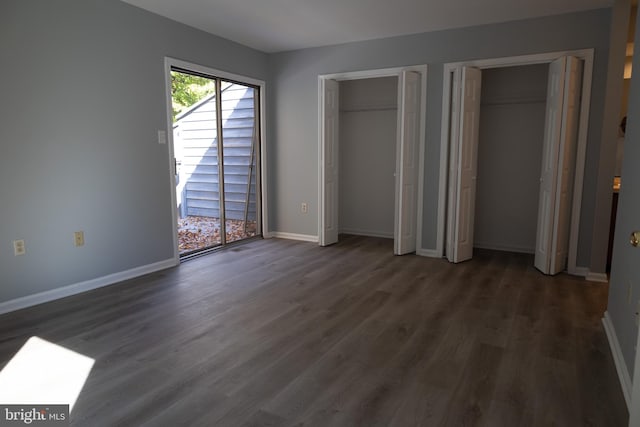 unfurnished bedroom with two closets and dark hardwood / wood-style flooring