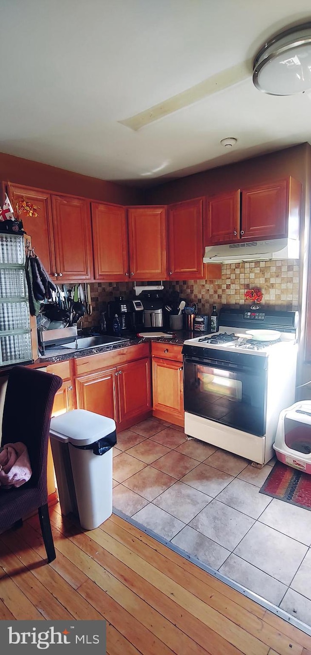 kitchen featuring white gas range oven, sink, light tile flooring, and backsplash