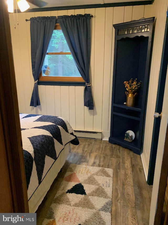 bedroom with dark hardwood / wood-style floors and a baseboard heating unit