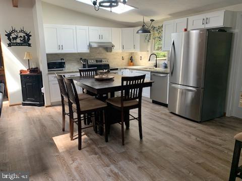 kitchen featuring vaulted ceiling, pendant lighting, white cabinetry, sink, and stainless steel appliances