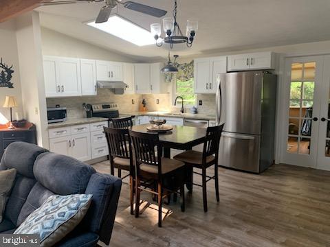 kitchen with lofted ceiling, white cabinetry, hanging light fixtures, dark hardwood / wood-style floors, and stainless steel appliances