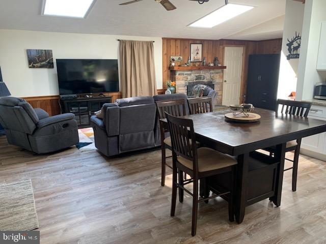 dining area with light hardwood / wood-style flooring, a stone fireplace, wooden walls, and ceiling fan