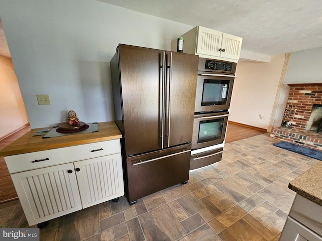 kitchen featuring fridge, white cabinetry, a fireplace, wooden counters, and double oven