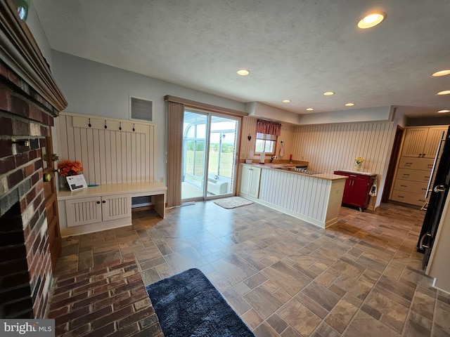 kitchen featuring a textured ceiling, a brick fireplace, a breakfast bar area, and kitchen peninsula