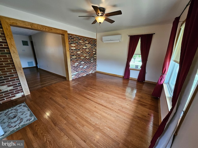 unfurnished room with brick wall, hardwood / wood-style floors, ceiling fan, and a wall mounted air conditioner