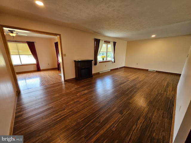 unfurnished room with a textured ceiling, baseboard heating, ceiling fan, and dark wood-type flooring