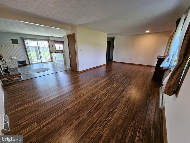 unfurnished living room featuring a textured ceiling, dark hardwood / wood-style flooring, and a brick fireplace