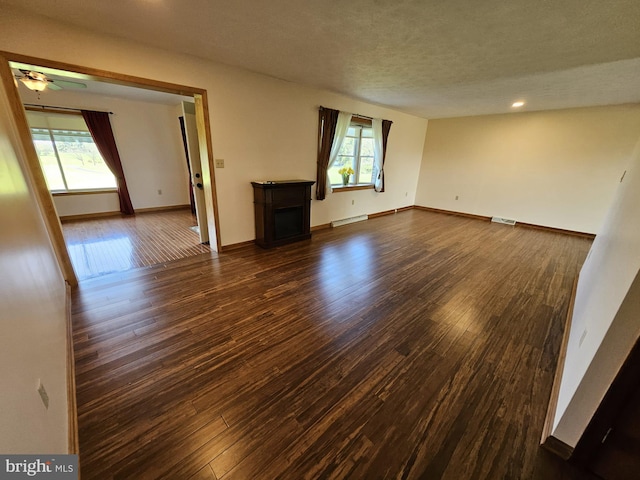 unfurnished living room with a baseboard heating unit, dark wood-type flooring, ceiling fan, and a healthy amount of sunlight