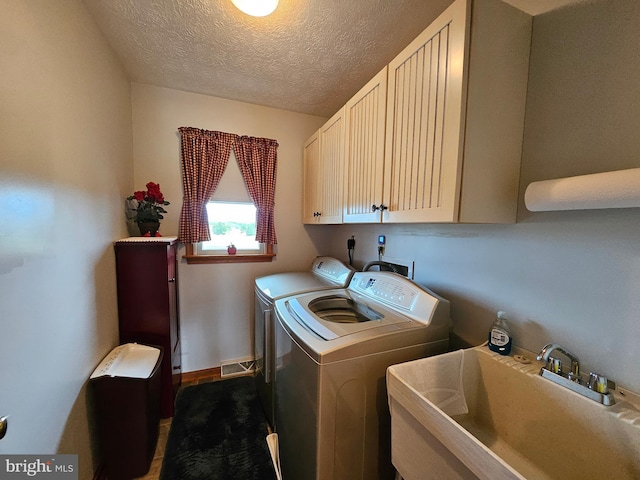 laundry room featuring a textured ceiling, washing machine and dryer, cabinets, and sink