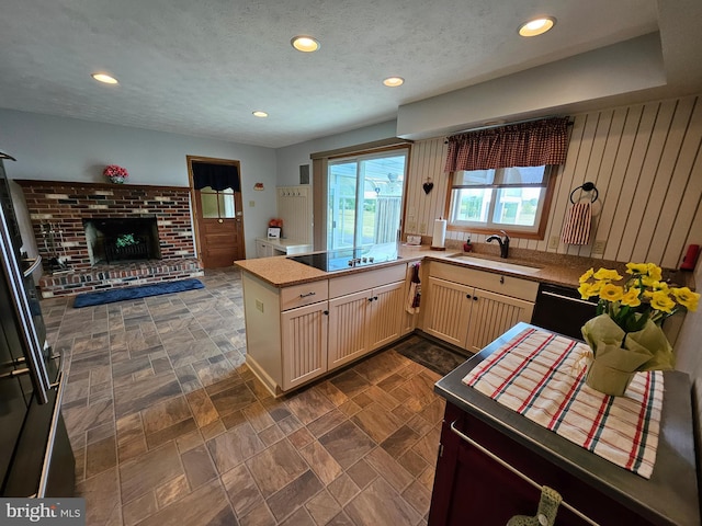 kitchen featuring sink, a textured ceiling, a fireplace, kitchen peninsula, and black appliances