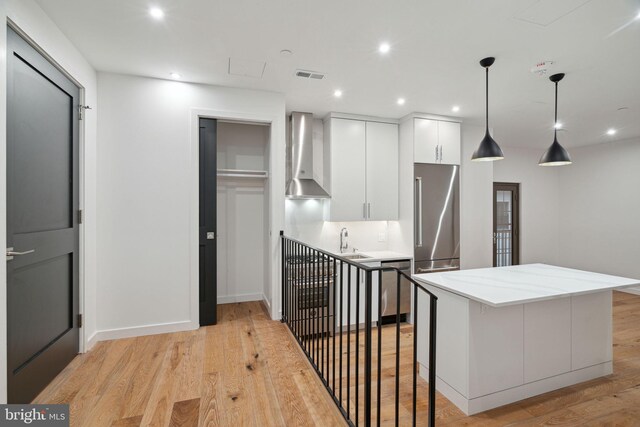 kitchen featuring a kitchen bar, appliances with stainless steel finishes, wall chimney exhaust hood, light hardwood / wood-style flooring, and white cabinetry