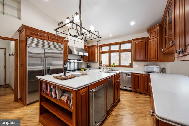 kitchen featuring wall chimney range hood, light hardwood / wood-style flooring, a notable chandelier, a center island, and appliances with stainless steel finishes