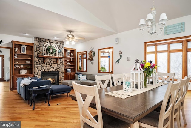 dining room featuring ceiling fan with notable chandelier, light hardwood / wood-style flooring, a fireplace, and vaulted ceiling