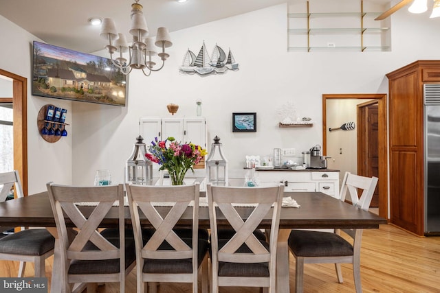 dining space with a notable chandelier, vaulted ceiling, and light hardwood / wood-style flooring