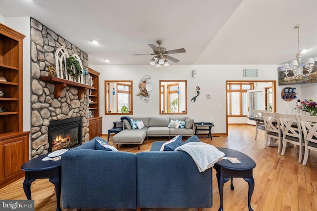 living room with ceiling fan with notable chandelier, light hardwood / wood-style floors, a fireplace, and a wealth of natural light