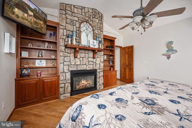 bedroom featuring lofted ceiling, a fireplace, light wood-type flooring, and ceiling fan