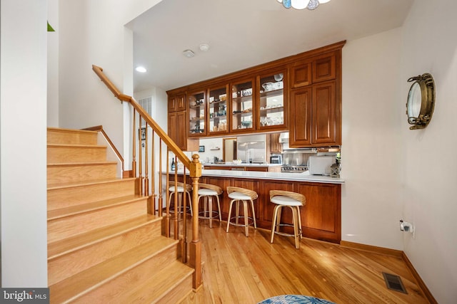 kitchen with kitchen peninsula, built in refrigerator, light wood-type flooring, and a kitchen bar