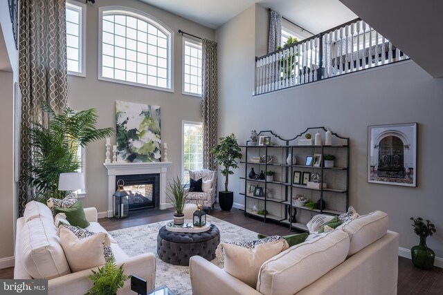 living area with dark wood-style flooring, a glass covered fireplace, a wealth of natural light, and baseboards