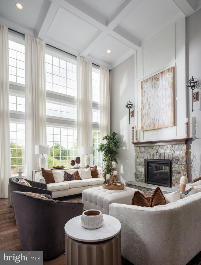 living room featuring coffered ceiling, dark wood finished floors, a towering ceiling, a stone fireplace, and a wealth of natural light