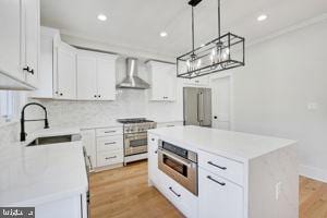 kitchen featuring a center island, wall chimney exhaust hood, stainless steel appliances, sink, and white cabinets