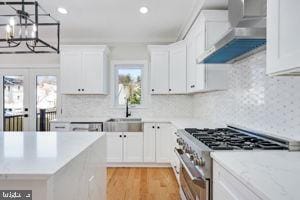 kitchen featuring french doors, wall chimney range hood, sink, high end stainless steel range oven, and white cabinetry