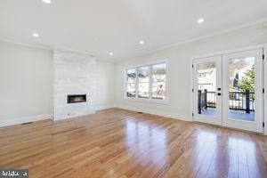 unfurnished living room featuring a large fireplace, light hardwood / wood-style floors, ornamental molding, and french doors