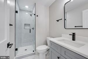 bathroom featuring a shower with door, vanity, and toilet