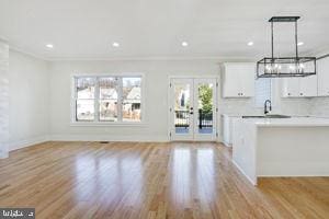 unfurnished living room featuring french doors, light hardwood / wood-style floors, ornamental molding, and sink