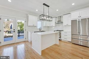 kitchen featuring french doors, white cabinets, wall chimney exhaust hood, decorative light fixtures, and stainless steel appliances