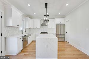 kitchen featuring tasteful backsplash, stainless steel appliances, crown molding, white cabinetry, and a kitchen island