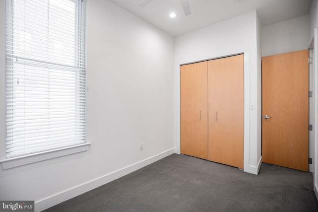 unfurnished bedroom with ceiling fan, dark carpet, and a closet