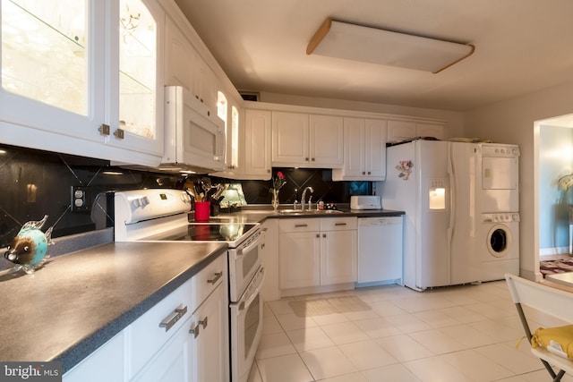 kitchen featuring tasteful backsplash, white appliances, stacked washing maching and dryer, light tile floors, and white cabinets