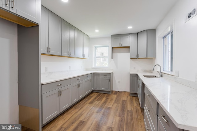 kitchen featuring light stone countertops, dark hardwood / wood-style flooring, gray cabinetry, and sink