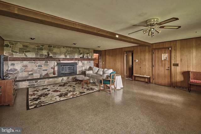 living room with a textured ceiling, a fireplace, beam ceiling, wood walls, and ceiling fan