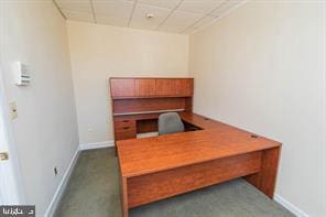 unfurnished office featuring dark carpet and a paneled ceiling