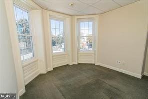 empty room featuring dark colored carpet, a wealth of natural light, and a paneled ceiling