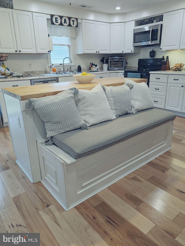 kitchen featuring wooden counters, black range with electric stovetop, sink, light hardwood / wood-style floors, and white cabinetry