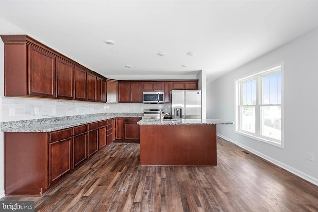 kitchen with light stone counters, stainless steel appliances, an island with sink, and dark wood-type flooring