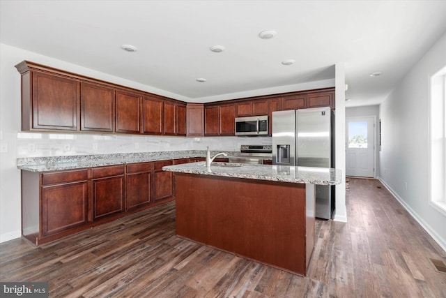 kitchen featuring sink, light stone counters, dark hardwood / wood-style floors, a center island with sink, and appliances with stainless steel finishes