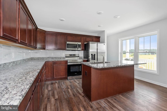 kitchen featuring dark wood-type flooring, a center island with sink, sink, light stone countertops, and stainless steel appliances